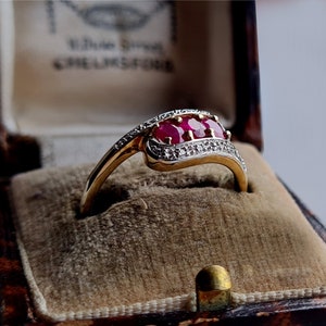 May include: A gold ring with three ruby stones and a diamond band. The ring is in a velvet ring box.