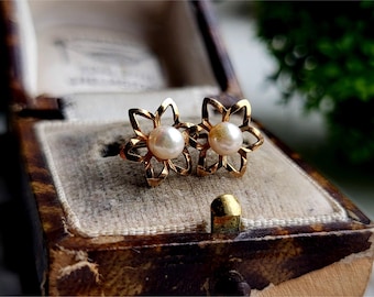 May include: A pair of gold flower-shaped earrings with a pearl in the centre of each flower.