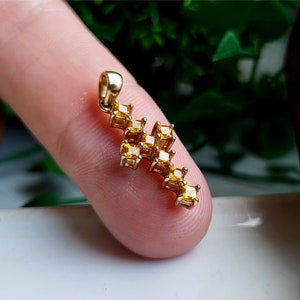 May include: A gold cross pendant with a cluster of small, square-shaped, yellow gemstones.