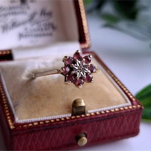 Può includere: Un anello vintage con un design a stella, con un gruppo di pietre preziose rosse. L'anello è incastonato in una fascia d'oro e presentato in un cofanetto rosso con interno color crema.
