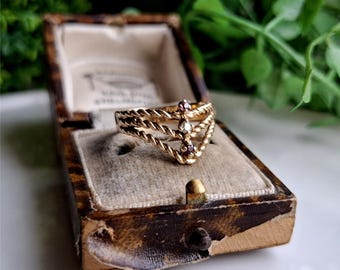May include: A gold ring with three twisted bands and three small gemstones. The gemstones are a clear diamond in the center and two pink stones on either side.