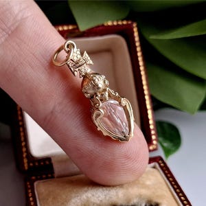 Peut inclure: Un pendentif doré avec une pierre claire taillée en forme de goutte. Le pendentif présente des détails ornés et une petite boucle en haut pour une chaîne. Le pendentif est présenté dans un écrin rouge.