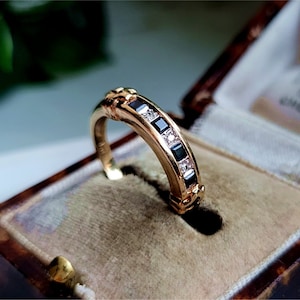 Op de afbeelding: Een gouden ring met een rij afwisselende zwarte en witte vierkante edelstenen.