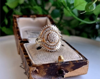 May include: A gold ring with a large round center stone surrounded by smaller diamonds. The ring is in a brown velvet ring box.