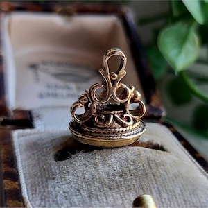 May include: A gold-toned metal seal with an ornate design. The seal is in a velvet-lined box.