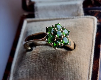 May include: A gold ring with a cluster of green gemstones set in a flower shape. The ring is in a velvet ring box.
