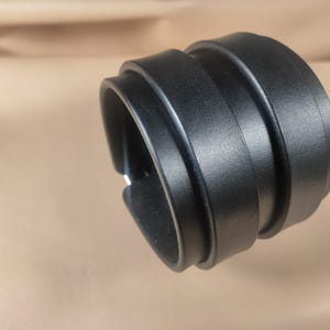 May include: A black leather cuff bracelet with a layered design. The bracelet is wide and wraps around the wrist, featuring a textured surface. The cuff is a bold accessory, suitable for various styles.