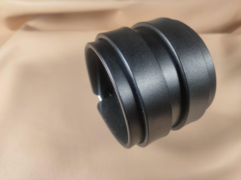 May include: A black leather cuff bracelet with a layered design. The bracelet is wide and wraps around the wrist, featuring a textured surface. The cuff is a bold accessory, suitable for various styles.