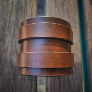 May include: A stacked leather cuff bracelet in a rich brown hue. The bracelet is composed of several horizontal bands of leather, creating a layered effect. The cuff is a bold accessory, perfect for adding a touch of rustic style.