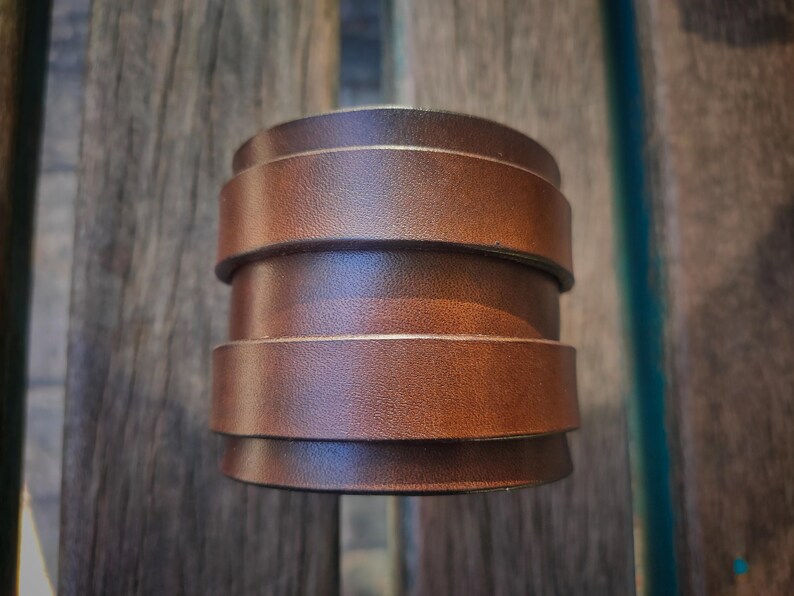 May include: A stacked leather cuff bracelet in a rich brown hue. The bracelet is composed of several horizontal bands of leather, creating a layered effect. The cuff is a bold accessory, perfect for adding a touch of rustic style.