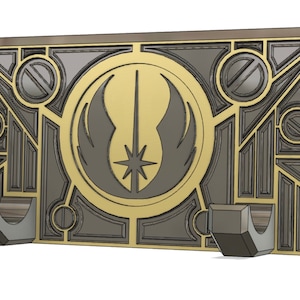 May include: A wall mount with a gold and grey design featuring the Jedi Order symbol. The mount has two hooks on the bottom.