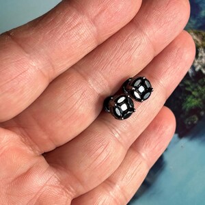 Op de afbeelding: Een paar zwarte diamant oorbelletjes met een zilveren setting. De oorbelletjes zijn klein en rond en zijn gezet in een eenvoudige, klassieke stijl.