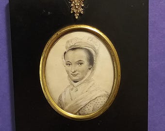 Puede incluir: Miniatura de retrato antiguo de una mujer con gorro y chal blancos, enmarcada en un óvalo. El retrato en blanco y negro está enmarcado por un borde dorado y un marco rectangular negro. Un elemento decorativo dorado corona el marco.