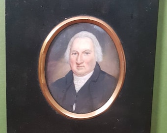 May include: A framed miniature portrait of a man with white hair, wearing a dark coat and white cravat. The portrait is set in an oval frame with a gold border.