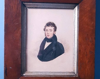 May include: A framed portrait of a man in a black coat and white collar. The portrait is in a simple wooden frame with a silver-colored inner border.
