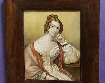 Puede incluir: Retrato en miniatura enmarcado en madera oscura, que representa a una mujer con vestido blanco y chal rojo. La mujer tiene cabello rizado castaño rojizo y apoya la barbilla en la mano. El fondo es amarillo suave y el marco tiene un lazo de metal.