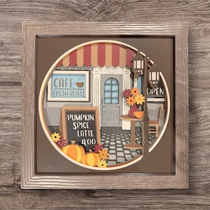 Könnte beinhalten: Eine Papiercraft-Szene eines Cafés mit einem roten Vordach, einem Schild mit der Aufschrift "Cafe Fresh Roast" und einem schwarzen Schild mit der Aufschrift "Pumpkin Spice Latte 4.00". Das Café ist in Herbstfarben dekoriert und hat einen Tisch und Stühle im Freien.