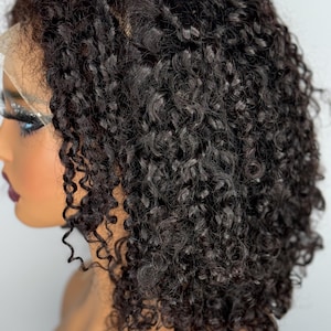 Puede incluir: Una peluca corta, rizada, negra con un frente de encaje. La peluca está diseñada en un bob con rizos sueltos.