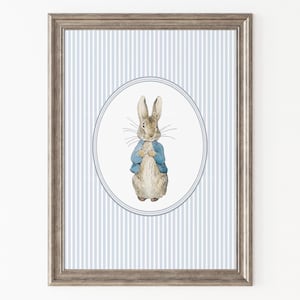 May include: A framed print with a watercolour illustration of a rabbit in a blue jacket, set against a blue and white striped background. The artwork is in a silver-toned frame, ideal for a nursery or children's room.