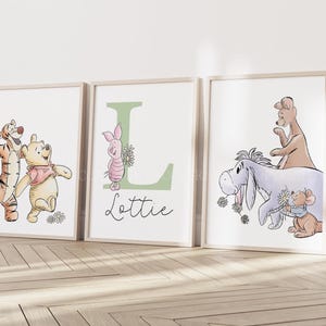 May include: Three framed wall art prints featuring Winnie the Pooh characters. The left print shows Tigger and Pooh. The center print features Piglet, a large green letter L, and the name Lottie. The right print shows Eeyore, Kanga, and Roo.