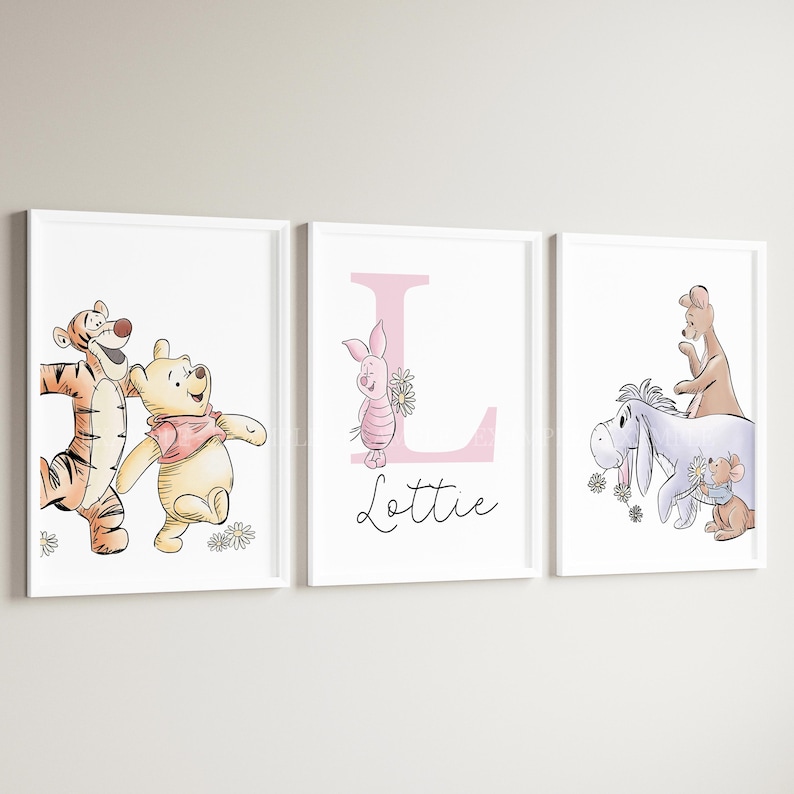 May include: Three white-framed wall prints featuring Winnie the Pooh characters. The left print shows Tigger and Pooh. The center print displays a large pink letter L, Piglet, and the name Lottie. The right print shows Eeyore, Roo, and Roo.