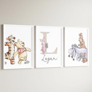 May include: Three framed wall art prints featuring Winnie the Pooh characters. The left print shows Tigger and Pooh. The center print features Piglet, a large letter L, and the name Logan. The right print shows Eeyore, Roo, and Roo.