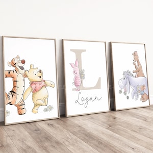 May include: Three framed wall art prints featuring Winnie the Pooh characters. The first shows Tigger and Pooh, the second features Piglet with a large letter L and the name Logan, and the third depicts Eeyore, Kanga, and Roo with flowers.