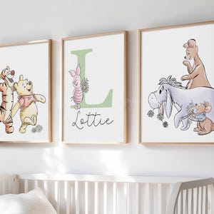 May include: Three framed wall art prints featuring Winnie the Pooh characters. The left print shows Tigger and Pooh. The center print displays a large green letter L with Piglet and the name Lottie. The right print shows Eeyore, Roo, and Roo.