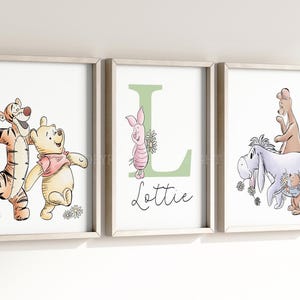 May include: Three framed wall art prints featuring Winnie the Pooh characters. The left print shows Tigger and Pooh, the centre print displays a large green letter L with Piglet and the name Lottie, and the right print shows Eeyore, Roo, and Roo.