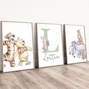 May include: Three framed wall art prints featuring Winnie the Pooh characters. The first shows Tigger and Pooh, the second a large green letter L with Piglet and the name Lottie, and the third Eeyore, Kanga, and Roo with daisies.