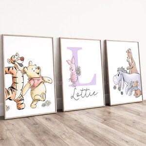May include: Three framed wall art prints featuring Winnie the Pooh characters. The first shows Tigger and Pooh, the second a large purple letter L with Piglet and the name Lottie, and the third Eeyore, Roo, and Roo's mother with flowers.
