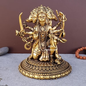 May include: A detailed golden statue of a deity with multiple arms and faces, holding various symbolic objects. The statue is on a decorative base, with the text "ADK Handicraft" visible. The background is a gradient of brown and gray.