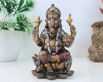 Puede incluir: Una estatua de Ganesha dorada y marrón sentada sobre una base de flor de loto. La estatua está decorada con acentos rojos, blancos y dorados. La estatua mide aproximadamente 15 cm de alto.