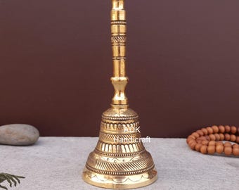 May include: A gold-colored bell with intricate designs on the bell and handle. The bell is sitting on a gray surface.