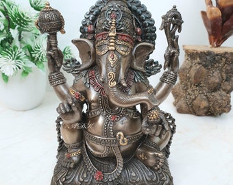 Könnte beinhalten: Eine detailreiche Bronzestatue von Ganesha, dem hinduistischen Gott der Weisheit und des Wohlstands. Die Statue zeigt aufwendige Schnitzereien und farbenfrohe Akzente, darunter Rot, Gold und Grün. Ganesha ist sitzend dargestellt, mit erhobenem Rüssel und einem kleinen Gegenstand in der Hand.