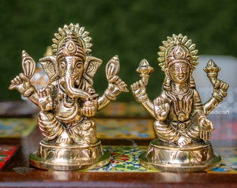 Peut inclure: Deux statues métalliques dorées de divinités hindoues, Ganesha et Lakshmi, assises sur une surface à motifs colorés. Les statues sont finement détaillées et de style indien traditionnel.