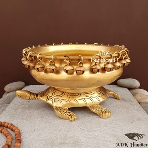 Pode incluir: Uma tigela de metal dourado com uma borda decorativa de sinos fica sobre uma base em forma de tartaruga. A tigela é feita de latão e tem um acabamento brilhante.