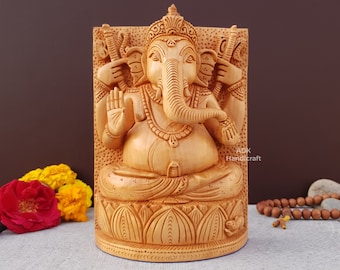 Op de afbeelding: Een handgesneden houten beeld van de hindoe-god Ganesha. Het beeld is geschilderd in een lichtbruine kleur en heeft ingewikkelde details. Het beeld zit op een lotusbloembasis.