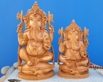 Op de afbeelding: Twee ingewikkeld gesneden houten beelden van de hindoe-god Ganesha. Het grotere beeld zit op een lotusbloem, terwijl het kleinere beeld op een muis zit. Beide beelden zijn gemaakt van lichtbruin hout en hebben een gedetailleerde afwerking.
