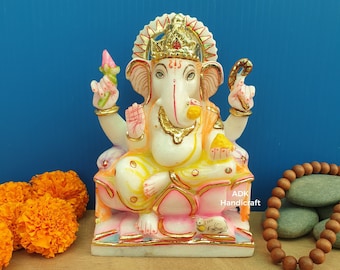 May include: White marble statue of Ganesha, the Hindu god of wisdom and prosperity, sitting on a lotus throne. The statue is decorated with gold paint and colorful accents. The statue is approximately 10 inches tall.
