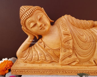 May include: A hand-carved wooden sculpture of a reclining Buddha. The sculpture is made of light brown wood and features intricate details. The Buddha is lying on its side with its head resting on its hand. The sculpture is on a wooden base.