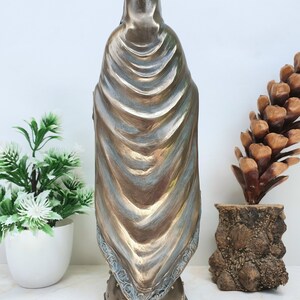 May include: A bronze statue of the Virgin Mary, wearing a blue robe and a crown. The statue is standing on a base with a star pattern and the text "2011 Veronese".