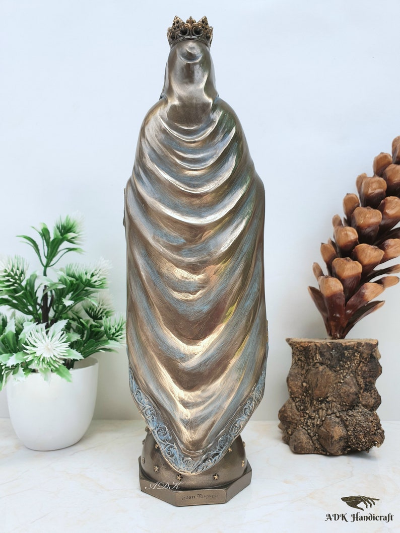 May include: A bronze statue of the Virgin Mary, wearing a blue robe and a crown. The statue is standing on a base with a star pattern and the text "2011 Veronese".