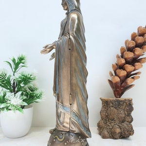 May include: A bronze-colored statue of the Virgin Mary, standing on a star-shaped base with a snake wrapped around it. The statue is wearing a crown and a long robe with blue accents. The statue is about 12 inches tall.
