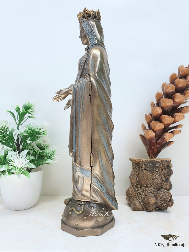 May include: A bronze-colored statue of the Virgin Mary, standing on a star-shaped base with a snake wrapped around it. The statue is wearing a crown and a long robe with blue accents. The statue is about 12 inches tall.