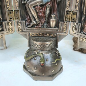 May include: A three-panel bronze sculpture depicting a scene from the Bible. The central panel shows a figure sitting on a throne with a snake at the base. The figure is holding a jar. The panels are hinged and can be opened and closed.