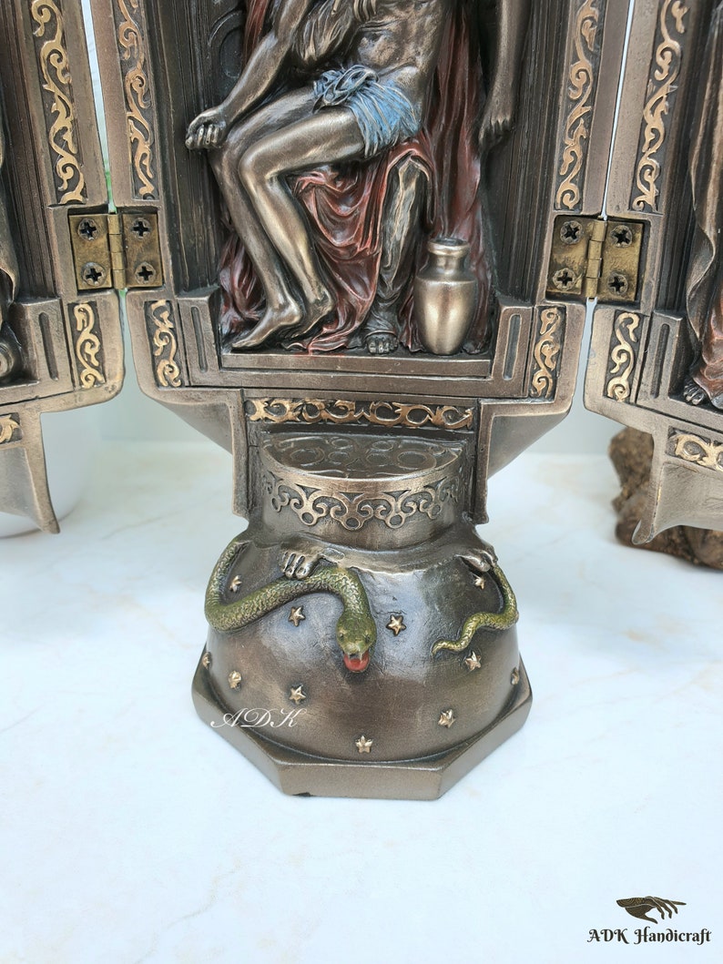 May include: A three-panel bronze sculpture depicting a scene from the Bible. The central panel shows a figure sitting on a throne with a snake at the base. The figure is holding a jar. The panels are hinged and can be opened and closed.