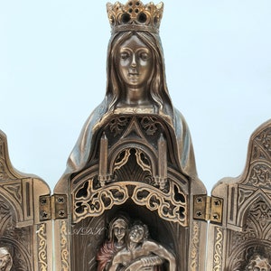 May include: A bronze-colored, three-panel folding altar with intricate carvings. The center panel features a sculpture of the Virgin Mary holding a figure of Jesus Christ. The left and right panels feature sculptures of saints.