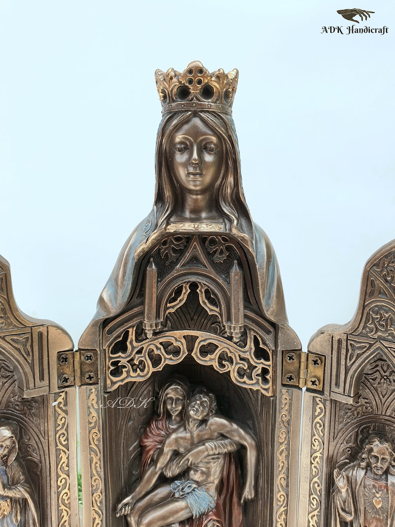 May include: A bronze-colored, three-panel folding altar with intricate carvings. The center panel features a sculpture of the Virgin Mary holding a figure of Jesus Christ. The left and right panels feature sculptures of saints.