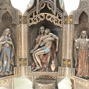 May include: A three-panel wooden altar with a gold-colored finish. The center panel features a sculpture of the Pieta, with Mary holding the body of Jesus. The left panel features a sculpture of Mary, and the right panel features a sculpture of Jesus with his heart exposed.